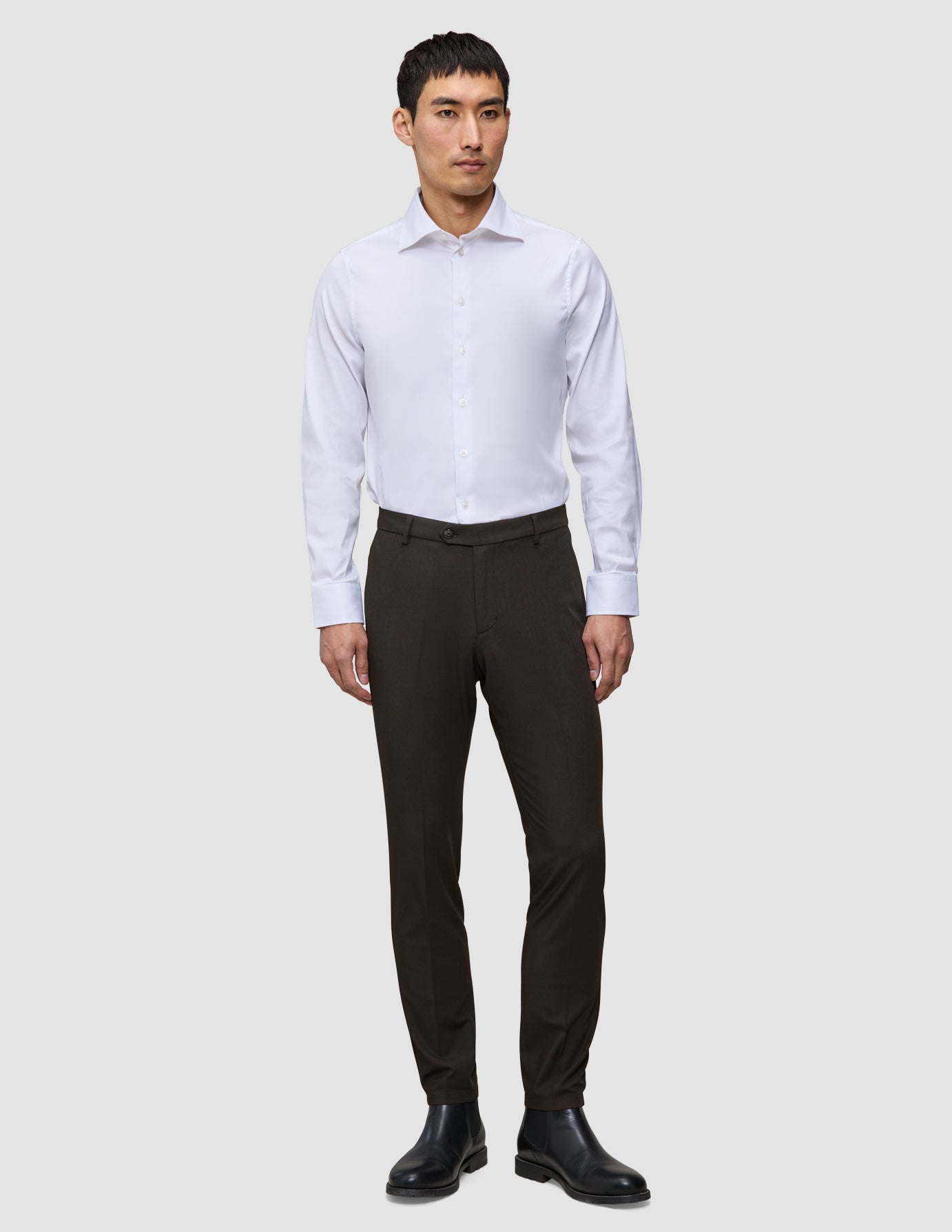 En man klädd i en vit skjorta, Motion Suit-byxor i modell Slim i färgen Cognac och svarta läderstövlar.